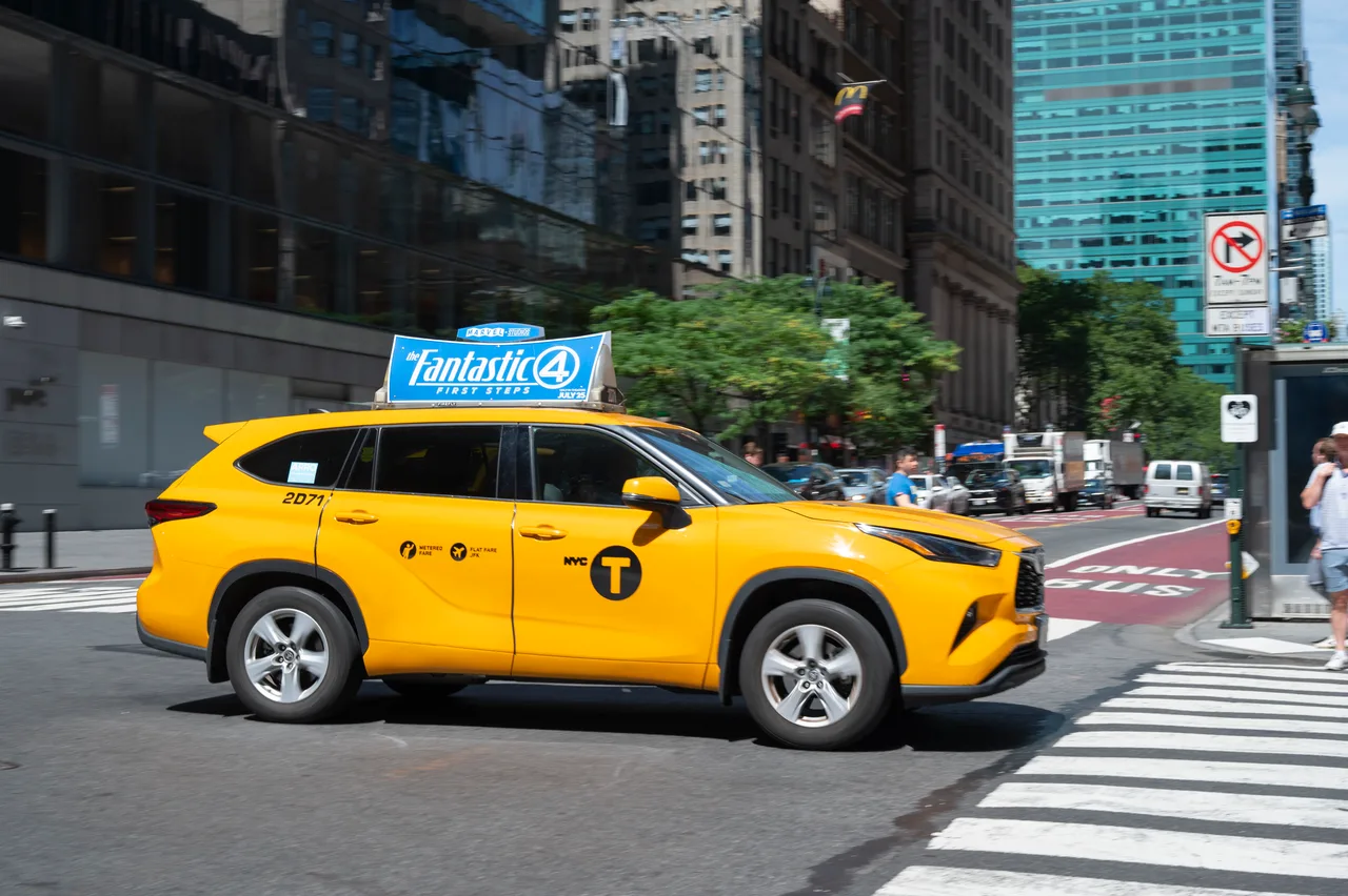 Yellow New York City taxi crossing a Manhattan intersection with a digital taxi-top screen running a Fantastic Four: First Steps campaign